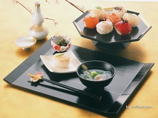 Preparate japoneze pe tăvi negre lăcuite, cu bețișoare și un bol de supă