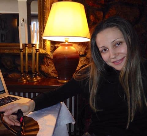 Femeie zâmbind la o masă, lângă un laptop și o veioză aprinsă