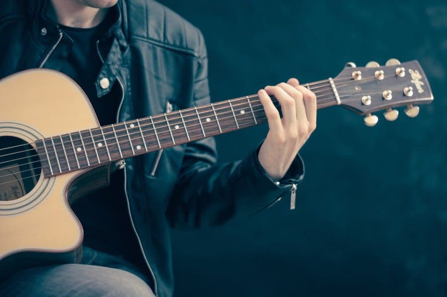Persoană în geacă de piele cântând la chitară acustică