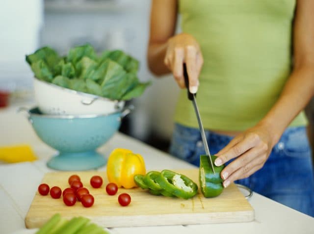 Femeie tăind ardei verde pe un tocător, lângă legume proaspete