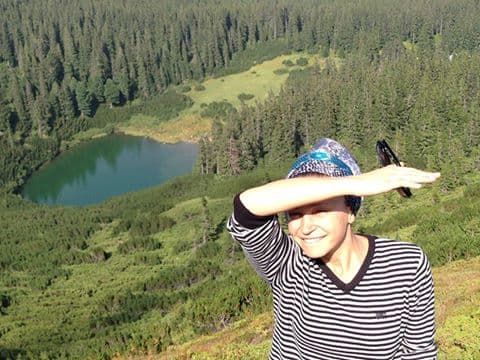 Femeie pe un versant împădurit, cu un lac de munte în spate