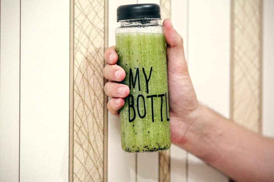 Mână care ține o sticlă cu smoothie verde, inscripționată „MY BOTTLE”