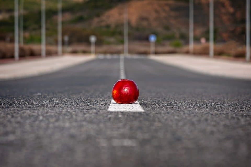 Măr roșu așezat pe linia albă a unui drum pustiu