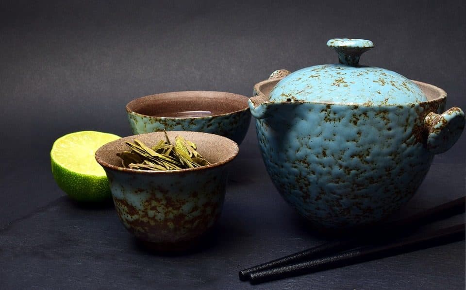 Ceainic turcoaz de ceramică, boluri cu frunze de ceai verde și jumătate de lime