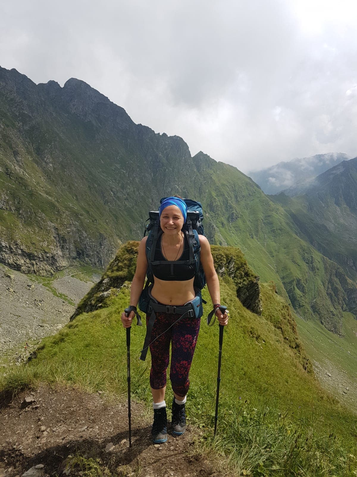 Femeie cu rucsac și bețe de trekking pe o potecă de munte