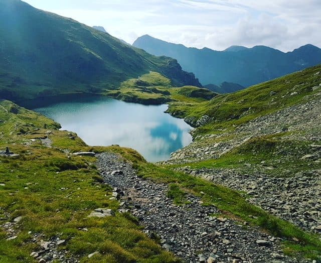 Lac alpin turcoaz și o potecă pietroasă printre pajiști