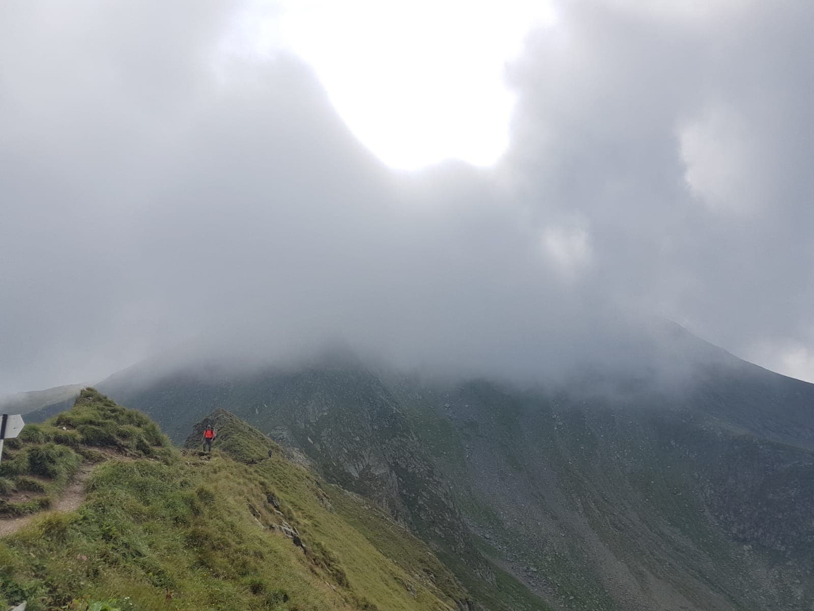 Creastă de munte în ceață, cu un drumeț în geacă roșie