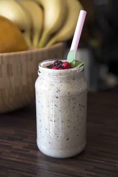 Borcan cu smoothie și fructe de pădure, lângă un coș cu banane