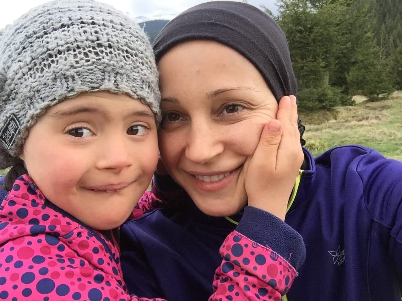 Femeie și fetiță cu căciuli, obraz lângă obraz, în natură