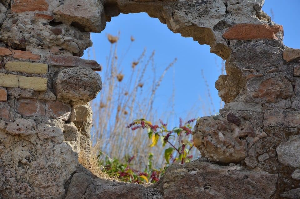 Deschizătură într-un zid de piatră, prin care se văd cerul și plante