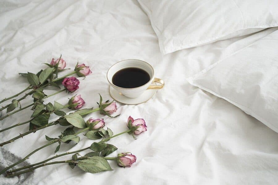Ceașcă de cafea și trandafiri roz pe un așternut alb