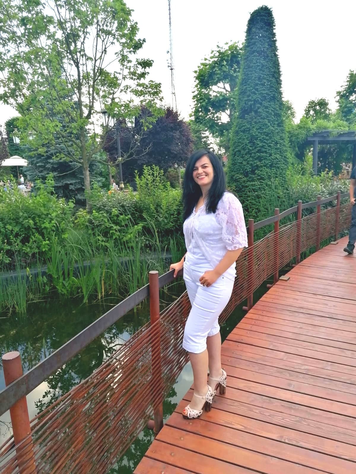 Femeie îmbrăcată în alb pe o punte de lemn din parc