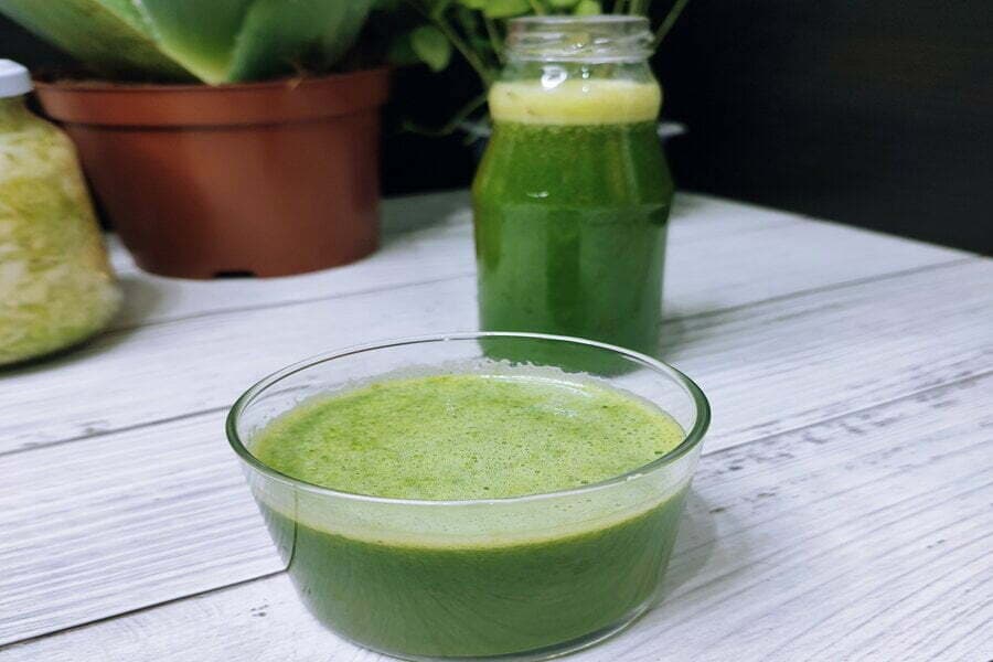 Bol și borcan cu suc verde pe o masă de lemn alb