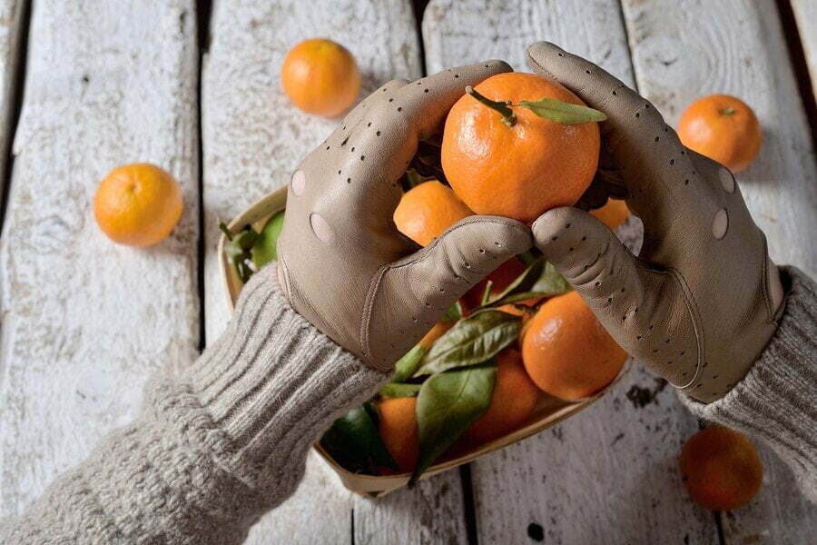 Mâini în mănuși ținând mandarine deasupra unui coș, pe lemn alb