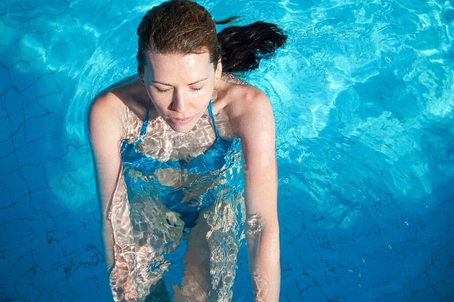 Femeie stând în apa albastră a unei piscine, văzută de sus