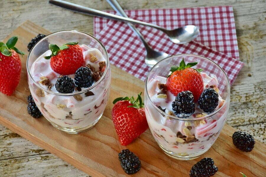 Două pahare cu iaurt, granola, căpșuni și mure
