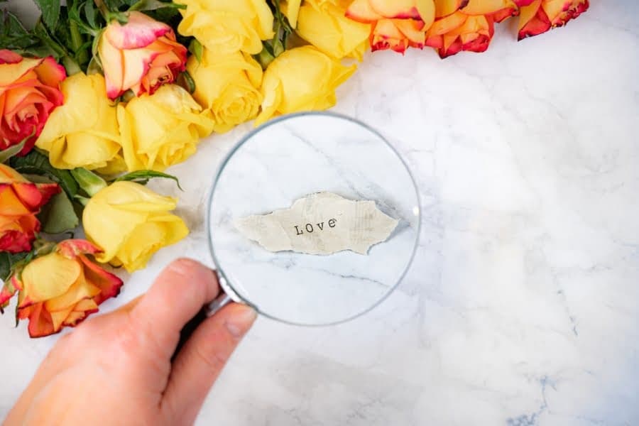Lupă peste o hârtie cu cuvântul „love”, lângă trandafiri galbeni