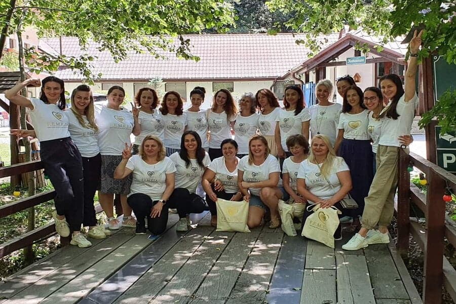 Grup de femei în tricouri albe, pe o punte de lemn, în aer liber