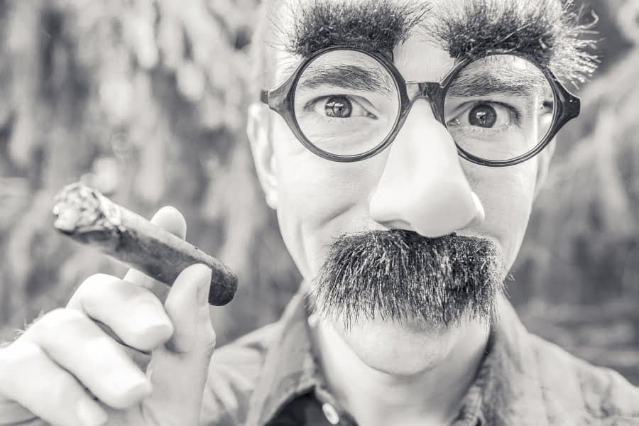 Portret alb-negru al unui bărbat cu ochelari, mustață falsă și trabuc
