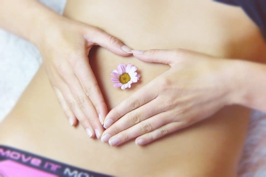 Mâini formând o inimă pe abdomen, cu o margaretă în mijloc