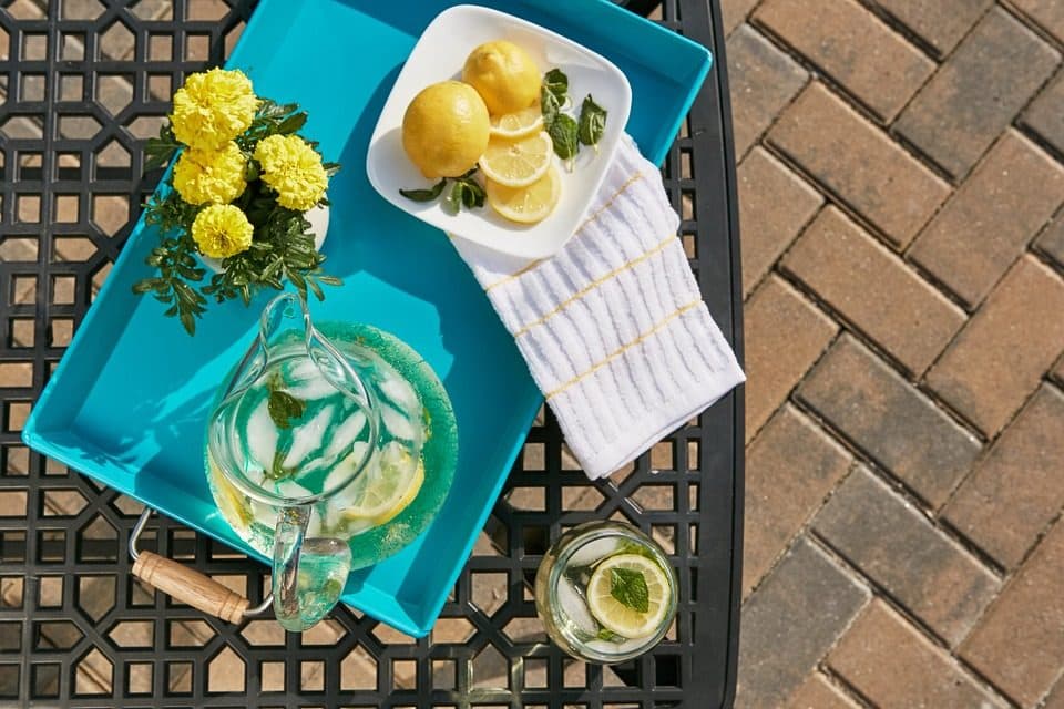 Tavă turcoaz cu limonadă, lămâi și flori galbene pe o masă de grădină