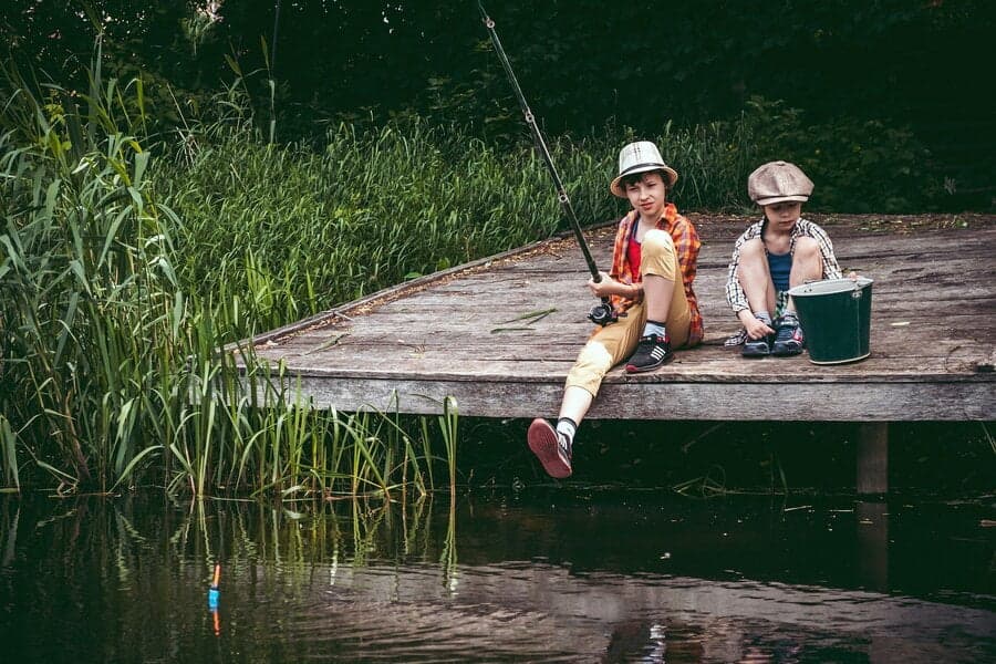 Doi copii pescuind pe un ponton de lemn lângă apă