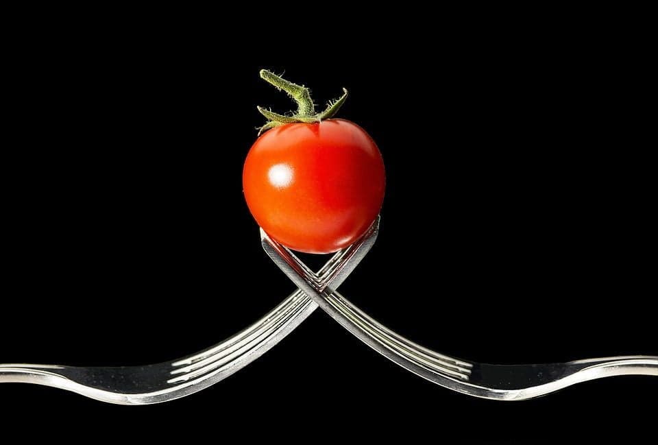 Roșie cherry așezată pe două furculițe încrucișate, fundal negru