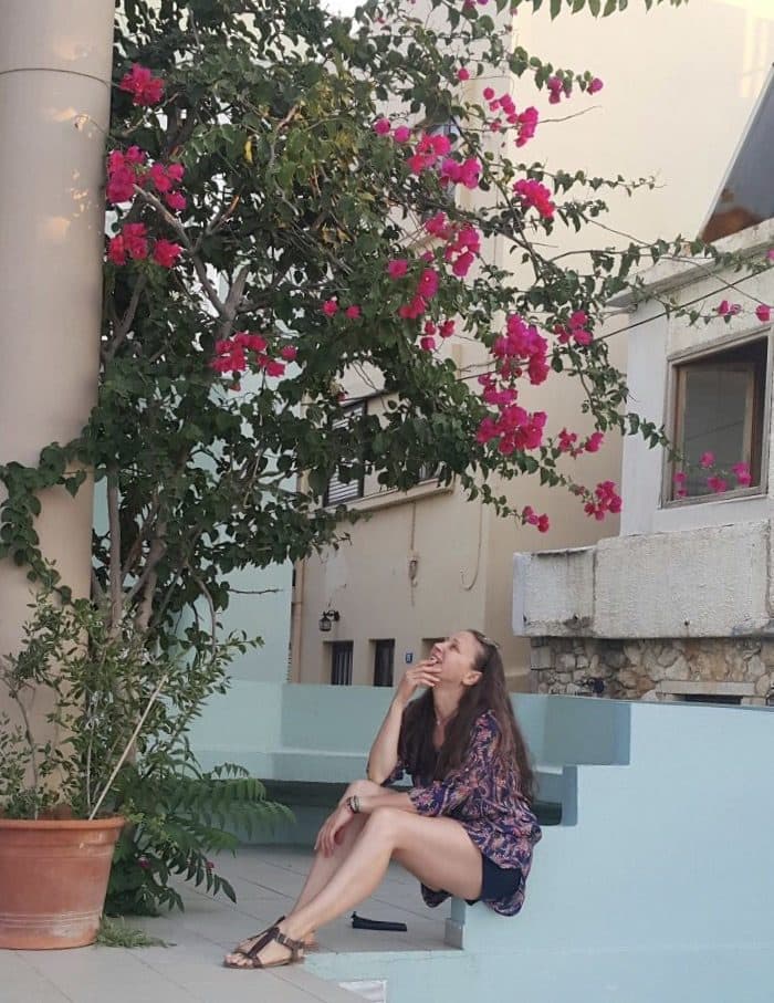 Femeie așezată pe trepte sub o bougainvillea înflorită, privind în sus