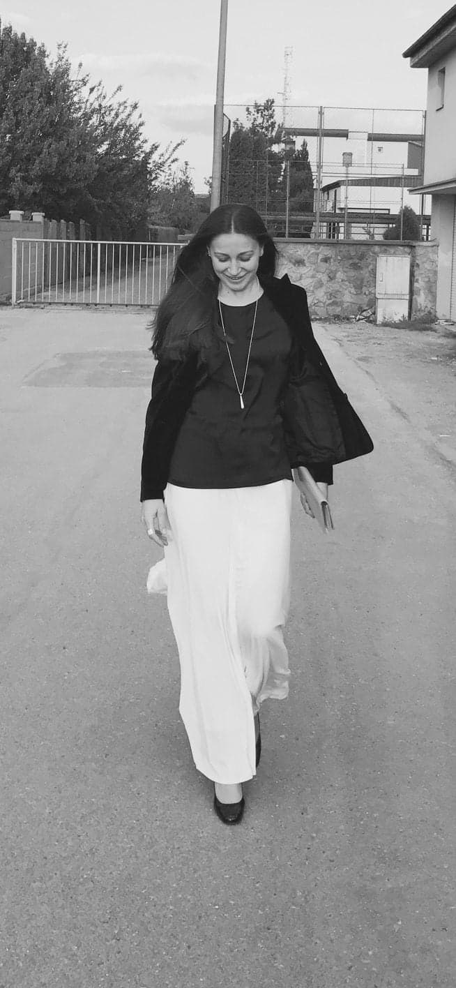 Fotografie alb-negru cu o femeie mergând pe stradă, în fustă lungă albă