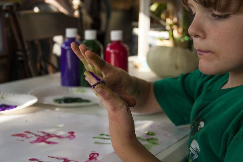 Copil cu palma vopsită, lângă sticle de tempera