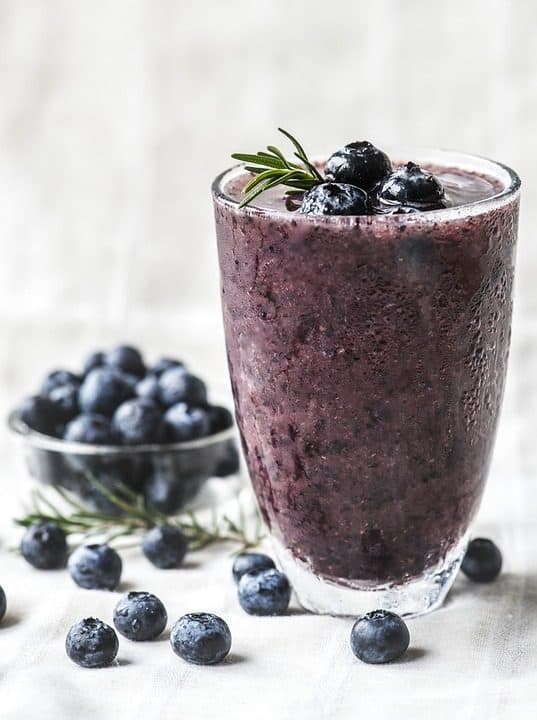 Pahar cu smoothie de afine, lângă un bol cu afine proaspete