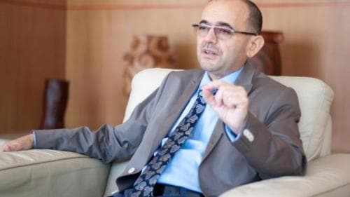 Bărbat în costum, așezat într-un fotoliu, gesticulând