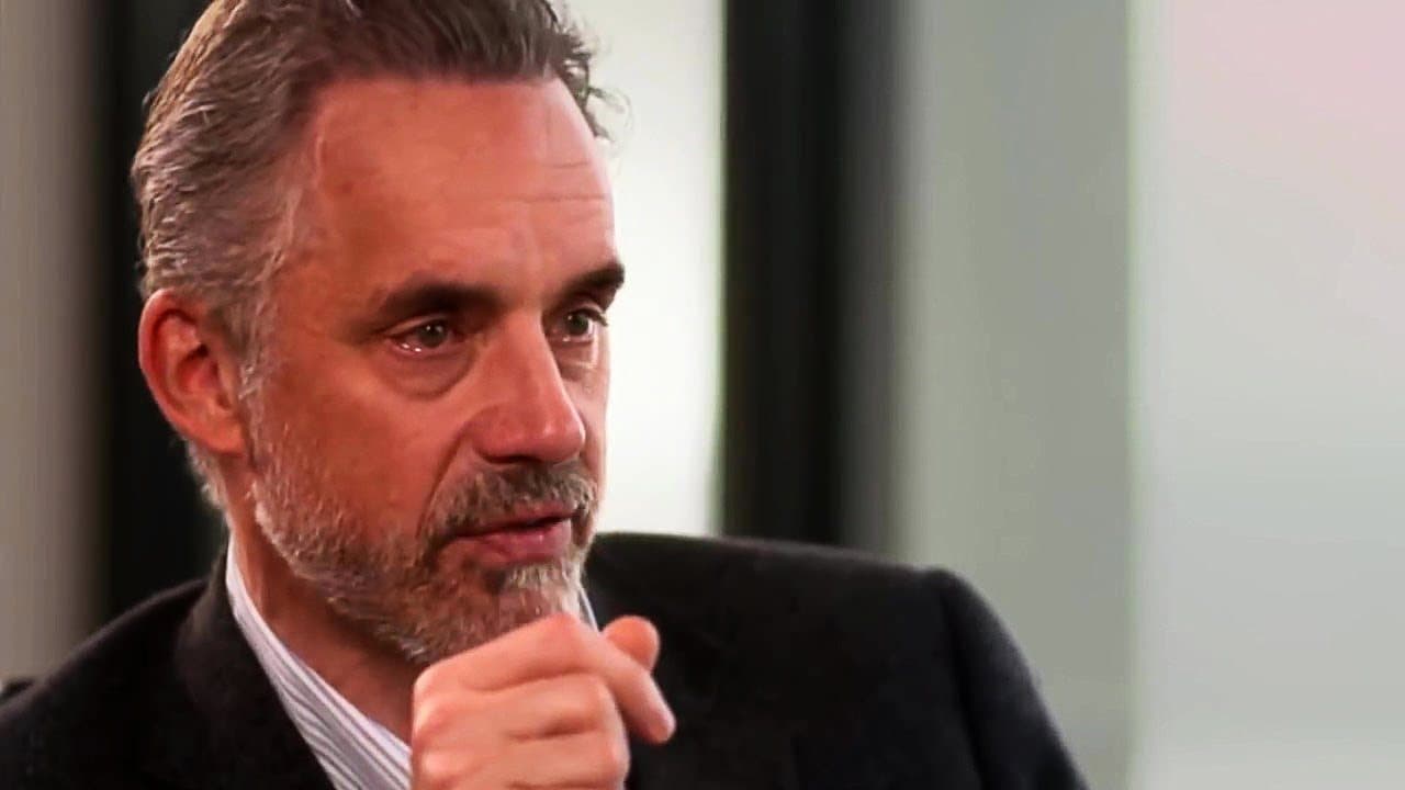 Bărbat cu barbă căruntă, cu mâna la bărbie, într-un cadru de interviu