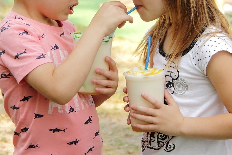 Doi copii bând din pahare cu paie, în aer liber