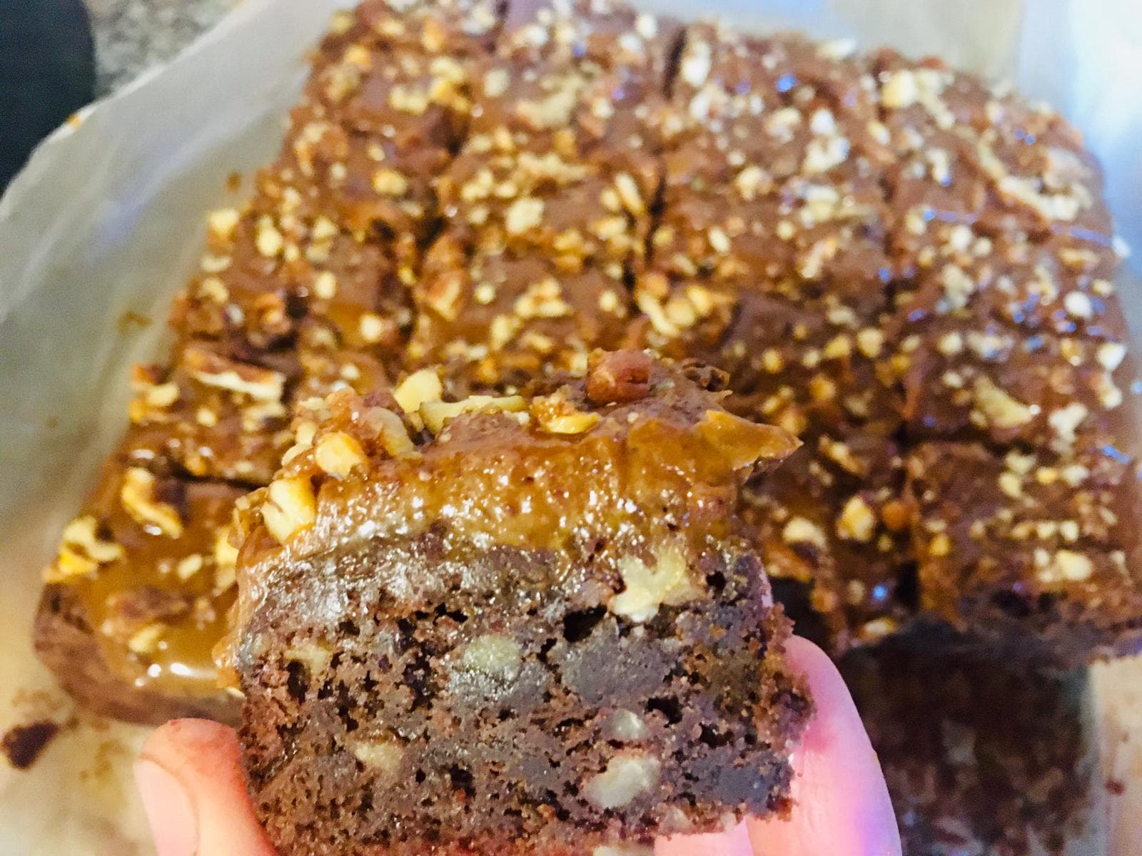 Mână ținând o bucată de brownie cu caramel și nuci