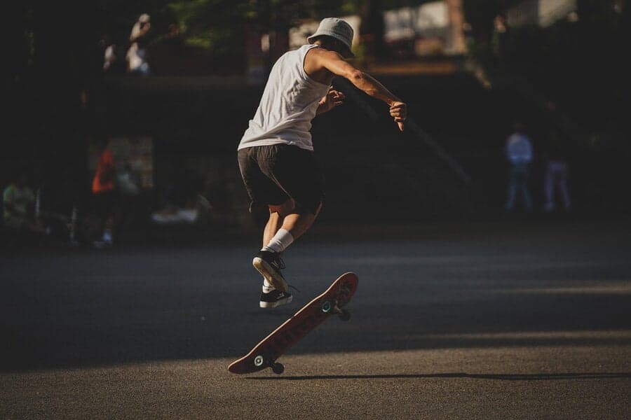 Tânăr cu pălărie sărind deasupra unui skateboard pe asfalt