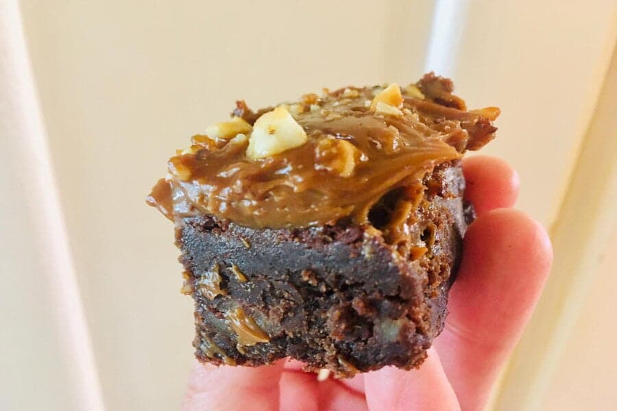 Bucată de brownie cu glazură de caramel, ținută în mână