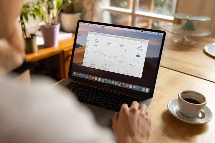 Persoană privind grafice pe laptop, lângă o ceașcă de cafea