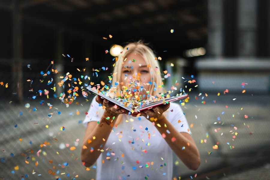 Femeie suflând confetti colorate dintr-o carte deschisă