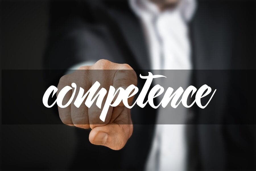Bărbat în costum arătând cu degetul, peste textul „competence”