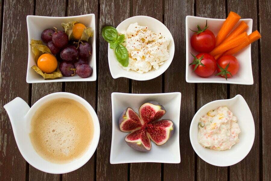 Șase boluri albe cu fructe, legume, brânză și cafea, pe lemn