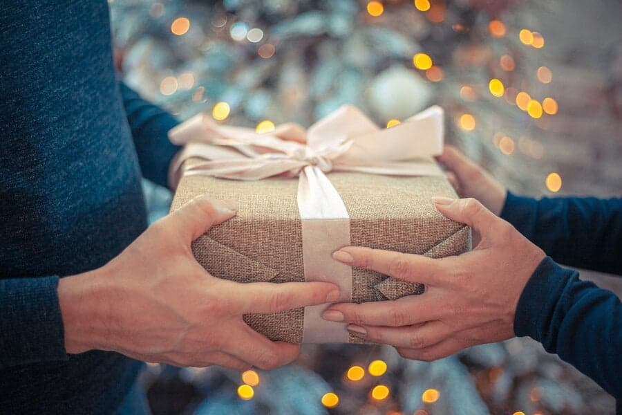 Mâini oferind o cutie-cadou cu fundă, pe fundal cu lumini
