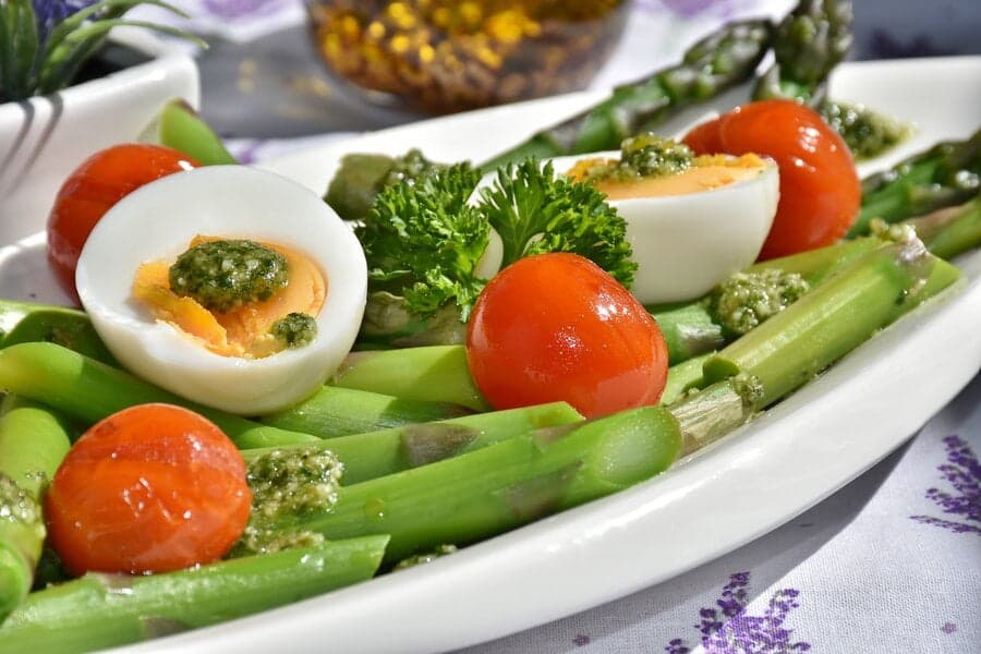 Sparanghel cu ouă fierte, roșii cherry și pesto pe o farfurie albă