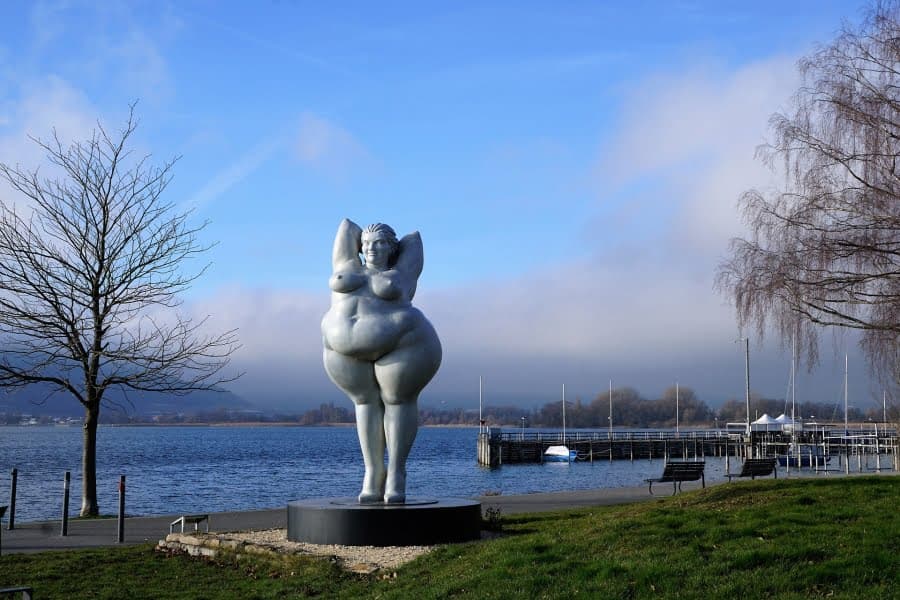 Statuie a unei femei corpolente pe malul unui lac