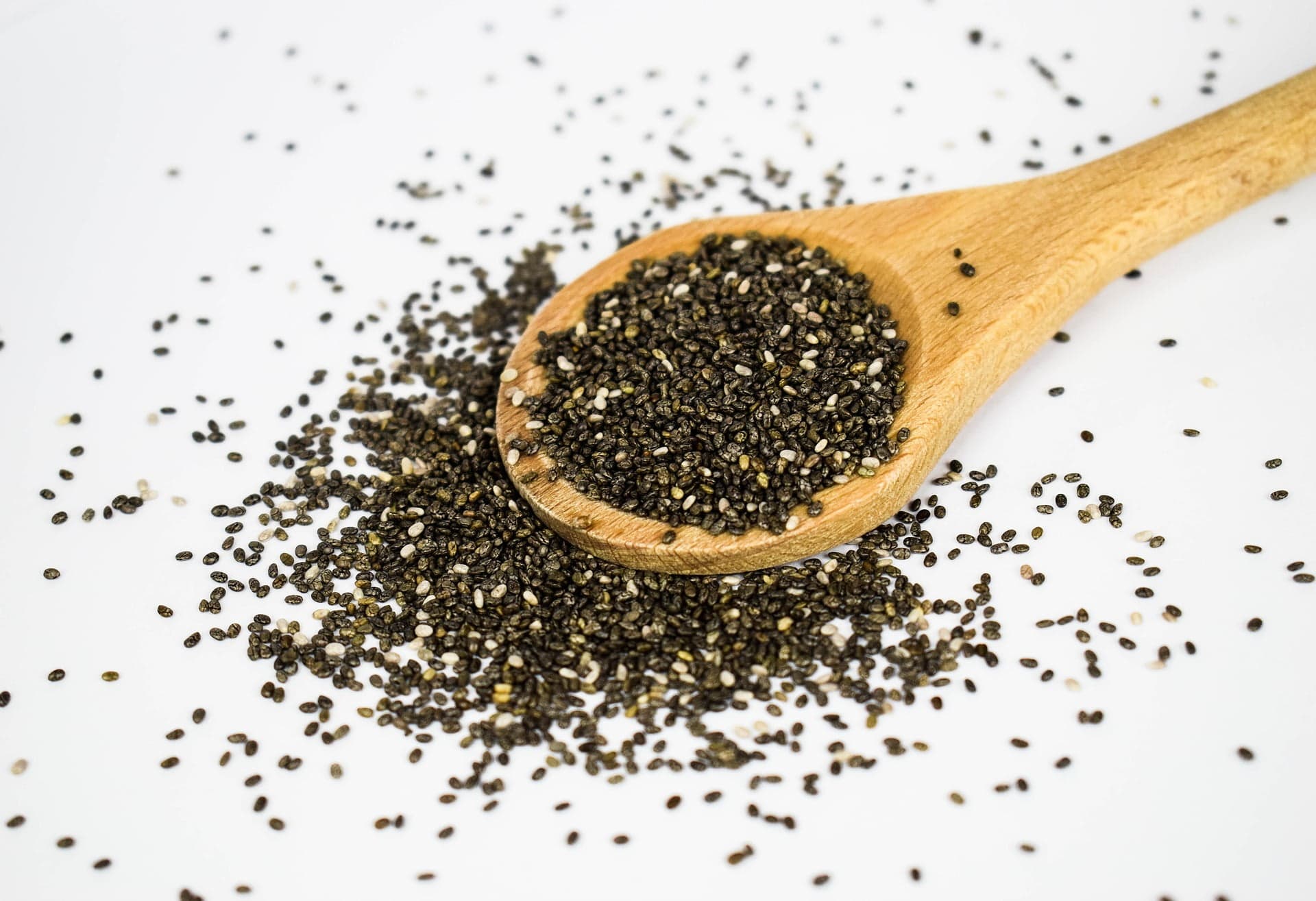 Semințe de chia pe o lingură de lemn, împrăștiate pe masă