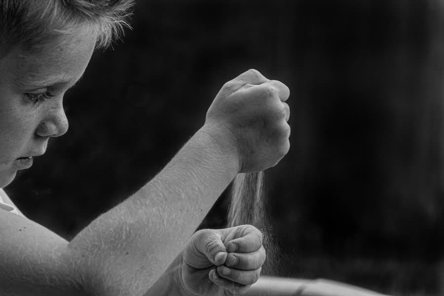 Portret alb-negru al unui băiat care lasă nisipul să curgă printre degete