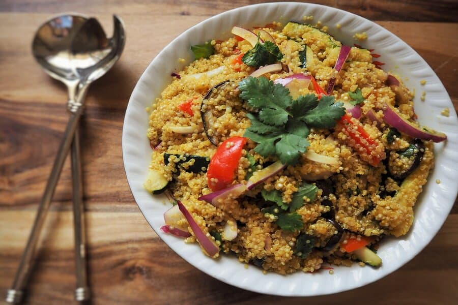 Bol alb cu quinoa și legume, lângă două linguri de servit