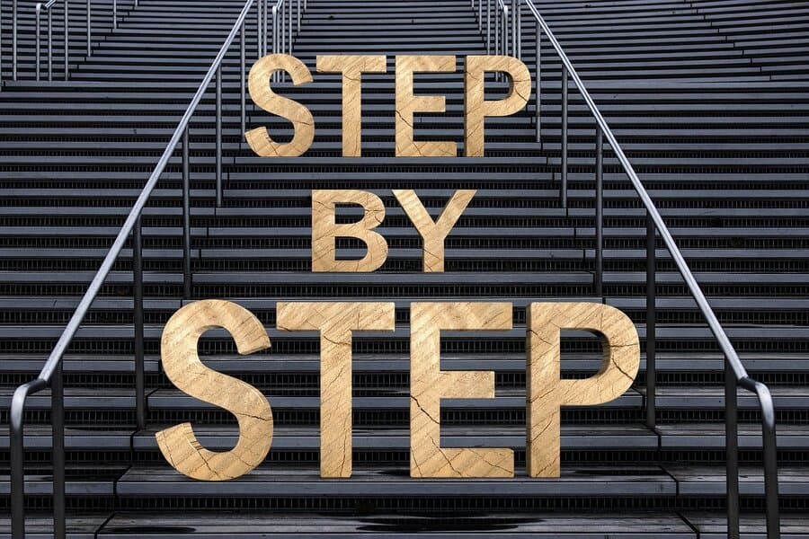 Litere mari de lemn cu textul „Step by step” pe o scară