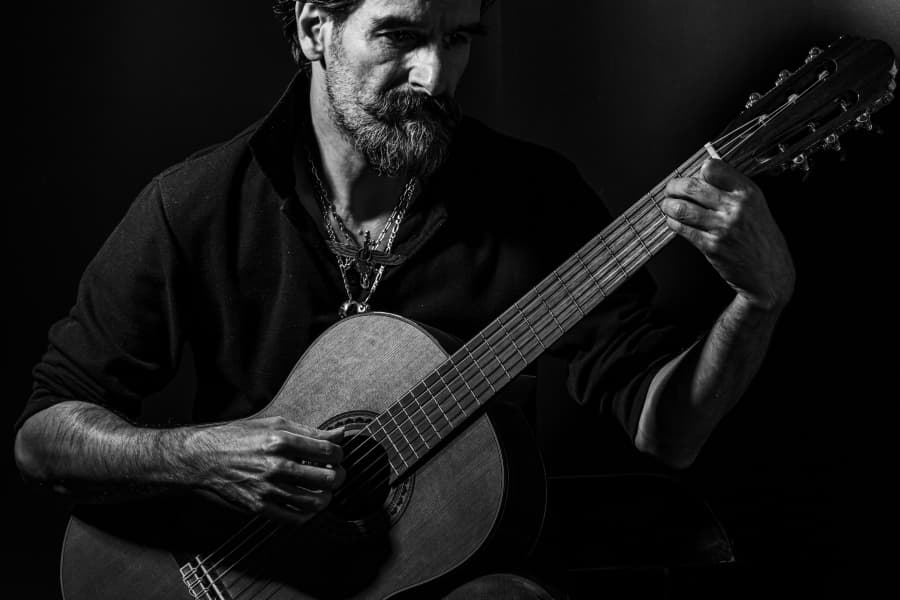 Portret alb-negru al unui bărbat cântând la chitară clasică