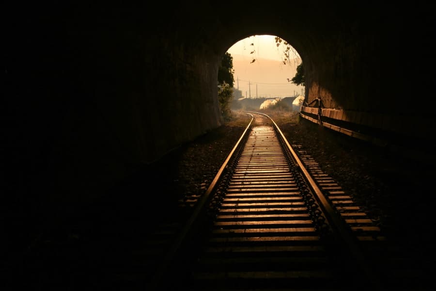 Șine de tren ieșind dintr-un tunel întunecat spre lumină